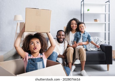 Excited African American Child Holding Cardboard Box Near Blurred Family