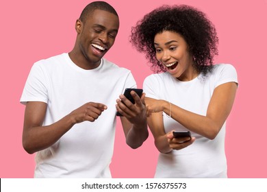 Excited African American couple using mobile phone, smiling laughing man and woman reading good news in social network or email, great shopping offer, online win, isolated on pink studio background - Powered by Shutterstock
