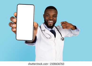 Excited African American Doctor Showing Smartphone With Blank Screen At Camera While Standing Over Blue Background, Black Medical Worker Pointing At Mobile Phone Screen, Recommending App, Mockup - Powered by Shutterstock