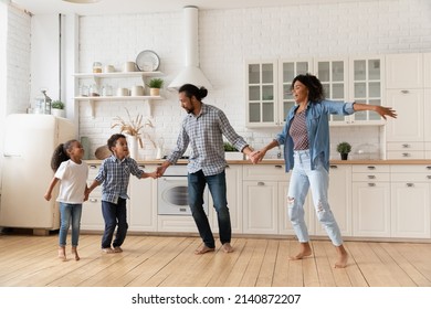 Excited African American Family Dancing To Music In Kitchen, Holding Hands, Singing, Enjoying Home Activity. Couple Of Parents And Sibling Kids Playing Active Games, Exercising, Having Fun