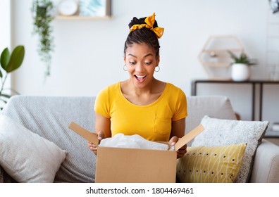 Excited african american girl unboxing cardboard delivery package, sitting at home, copy space