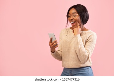 Excited African American Girl Using Smartphone Holding Finger On Chin Standing Over Pink Studio Background. Empty Space