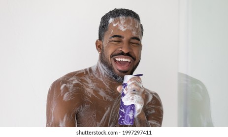 Excited African American guy in foam taking shower, singing to music, holding gel, shampoo bottle like microphone, having fun while enjoying morning bath. Male beauty care, hygiene concept - Powered by Shutterstock