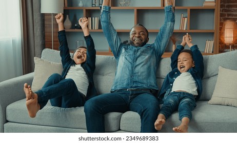 Excited African American happy family father and two siblings boys kids children fans watch TV sport game championship celebrate goal television team victory in sport match sit on sofa cheer together - Powered by Shutterstock