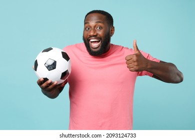 Excited African American Man Football Fan In Pink T-shirt Isolated On Blue Wall Background. Sport Family Leisure Lifestyle Concept. Cheer Up Support Favorite Team With Soccer Ball, Showing Thumb Up