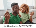 excited african american man in hearing aid device sitting near happy girlfriend in braces