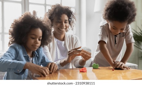 Excited african American mom or nanny have fun engaged in creative activity with little kids, happy biracial mother play with plasticine playdough, enjoy weekend with small children, hobby concept - Powered by Shutterstock