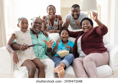 Excited African American Parents, Grandparents And Grandchildren On Couch Watching Tv And Cheering. Happy Three Generation Family Spending Time Together At Home.