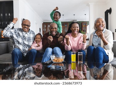 Excited african american parents, son, daughter and grandparents watching sport on tv, slow motion. Sport, entertainment, home, family, togetherness, domestic life and lifestyle, unaltered. - Powered by Shutterstock