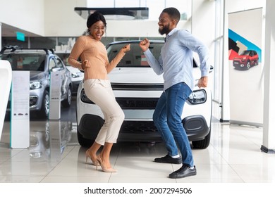 Excited African American Spouses Dancing In Dealership Office After Buying New Car, Cheerful Black Couple Having Fun In Auto Showroom, Celebrating Purchasing Family Automobile, Free Space