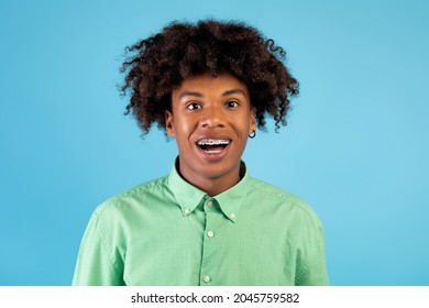 Excited African American Teen Guy With Braces Looking And Smiling At Camera, Wearing Shirt, Posing Isolated Over Blue Studio Background. Happy Male Teenage Model Portrait