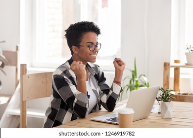 Excited African American woman in glasses read good news online at laptop, happy black female get promotional letter or email celebrating goal achievement, smiling girl look at computer lucky with win