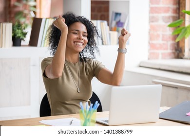 Excited african American woman sit at desk feel euphoric win online lottery, happy black woman overjoyed get mail at laptop being promoted at work, biracial girl amazed read good news at computer