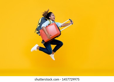 Excited African American woman tourist woman with backpack and luggage jumping in mid-air studio shot isolated on colorful yellow background