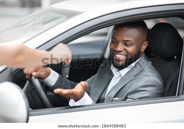 Excited\
african american young businessman sitting in brand new car, taking\
automatic key from car dealer hands. Smiling black man in suit\
taking his car from parking, closeup, copy\
space