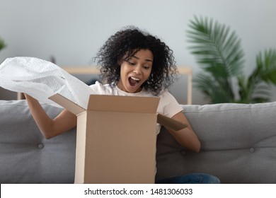 Excited african American young woman sit on couch at home unpack cardboard box shopping online, overjoyed black millennial girl buyer feel euphoric open shipped package parcel from delivery service - Powered by Shutterstock