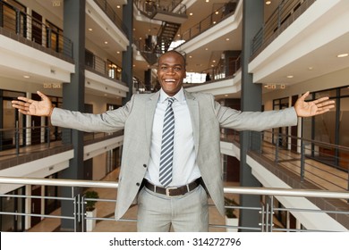 excited african businessman with arms outstretched in modern office building