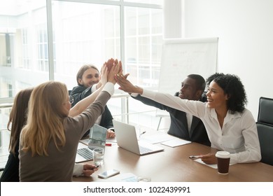 Excited african and caucasian business team giving high five at office meeting motivated by victory, achievement or good work result, multi-ethnic employees group celebrate corporate success together