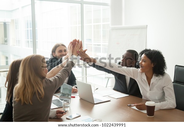 Excited african and caucasian business team\
giving high five at office meeting motivated by victory,\
achievement or good work result, multi-ethnic employees group\
celebrate corporate success\
together