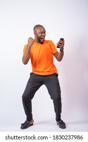 Excited African Man Celebrates While Looking At His Phone, Standing Against A White Background