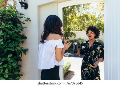 Excited african woman attending a female friend's housewarming party. Woman giving a wine bottle her friends at entrance door. - Powered by Shutterstock