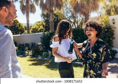 Excited african woman attending a friend's housewarming party. Woman giving a wine bottle to couple outdoors. - Powered by Shutterstock