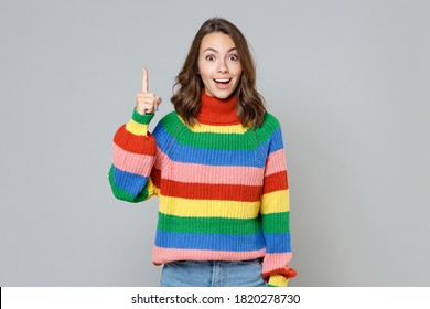 Excited amazed beautiful young brunette woman 20s wearing casual colorful knitted sweater holding index finger up with great new idea looking camera isolated on grey colour background studio portrait