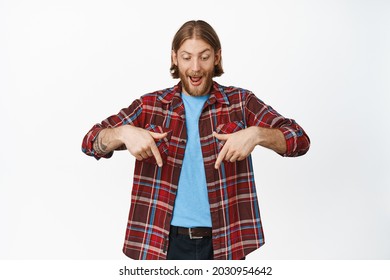 Excited And Amazed Blond Adult Man, Pointing And Looking Down With Thrilled Face Expression, Checking Out Awesome News, Stare In Awe, Standing Against White Background