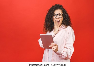 Excited Amazed Young Beautiful Woman With Tablet Pc. Happy Girl In White Shirt Using Tablet Computer, Isolated On Red Background. 