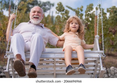 Excited Amazed Young Grandson And Old Grandfather Swinging In Spring Garden. Grand Dad And Grandson Having Fun On A Swing Together In Summer Garden. Active Summer Kids Leisure. Weekend With Granddad.