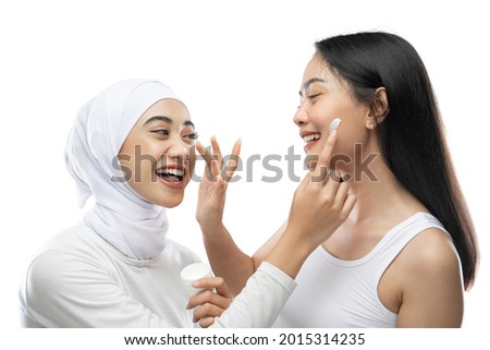 excited asian bestfriend applying face cream with finger hands against gray background