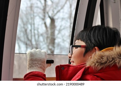 Excited Asian Boy Looking Outside The Window Of The Cable Car In Winter.