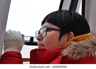 Excited Asian Boy Looking Outside The Window Of The Cable Car In Winter.