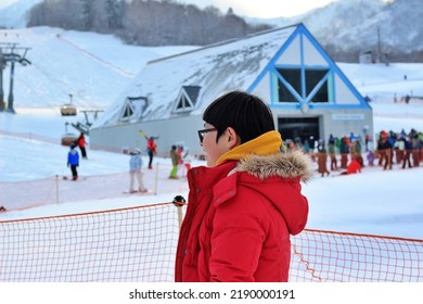 Excited Asian Boy Watching Other People Skiing At Ski Resort In Winter.