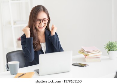 Excited Asian business woman after searching a job with a laptop at the office. Successful female wear glasses with victory gesture at the white room. Celebration.