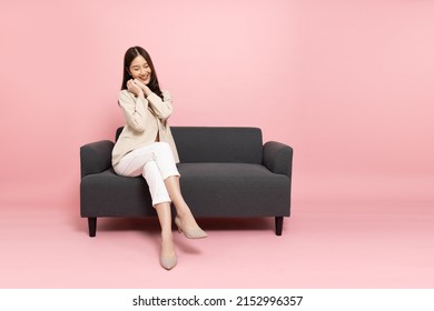 Excited Asian businesswoman sitting on sofa isolated on pink background