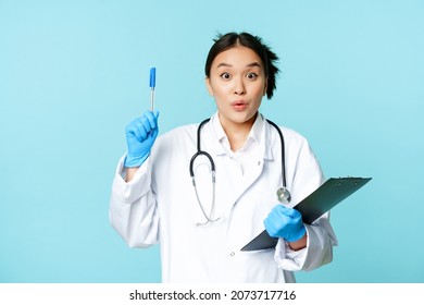 Excited Asian Female Physician Holding Clipboard, Raising Pen Up In Eureka Sign, Has Revelation, Pitching An Idea, Standing On Blue Background