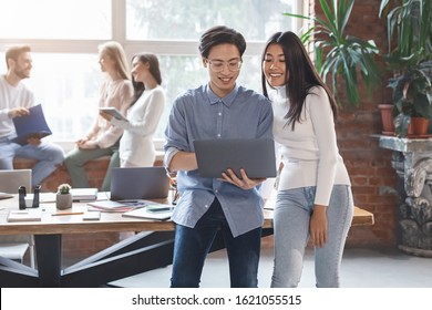 Excited Asian Guy Sharing Business Ideas With Young Mixed Race Woman Coworker, Man And Woman Looking At Laptop Screen, Office Interior