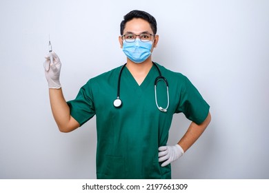 Excited Asian Male Nurse In Medical Mask, Rubber Gloves And Scrubs, Looking Amazed At Syringe With Vaccine, Isolated Over White Background