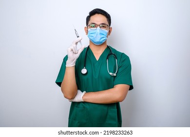 Excited Asian Male Nurse In Medical Mask, Rubber Gloves And Scrubs, Looking Amazed At Syringe With Vaccine, Isolated Over White Background