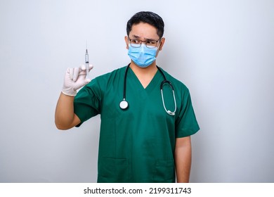 Excited Asian Male Nurse In Medical Mask, Rubber Gloves And Scrubs, Looking Amazed At Syringe With Vaccine, Isolated Over White Background