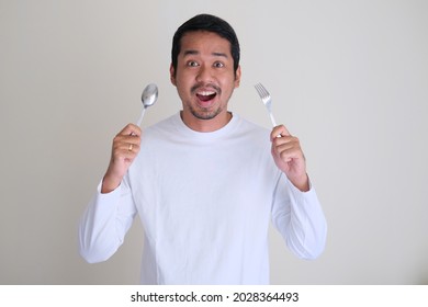 Excited Asian man holding spoon and fork in his hands