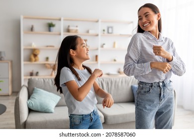 Excited Asian Mom And Cute Daughter Dancing To Music And Having Fun At Home, Smiling To Each Other. Young Mother And Her Kid Fooling Around And Enjoying Favorite Song Together