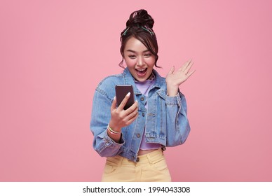 Excited Asian Woman Celebrating With Mobile Phone Isolated Over Pink Background.