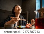 Excited Asian woman eating tasty sushi set with shrimps and tobiko roe