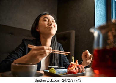 Excited Asian woman eating tasty sushi set with shrimps and tobiko roe - Powered by Shutterstock