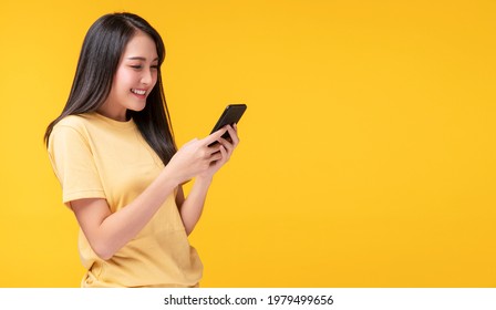 Excited asian woman holding mobile phone on yellow background isolated. Cheerful girl young asian woman holding smartphone in hands smile with teeth happy face. Exciting Women Online Shopping concept. - Shutterstock ID 1979499656
