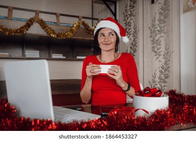 Excited Asian Woman Holding And Opening Christmas Present, Smiling Lady Unwrapping Gift Box, Sitting On The Table At Home In Living Room With Laptop Computer, Celebrating Online