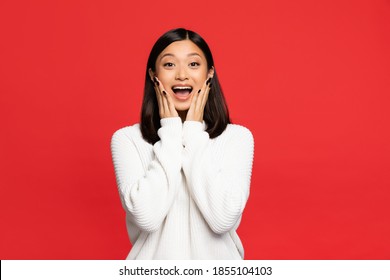 Excited Asian Woman With Open Mouth Touching Cheeks Isolated On Red