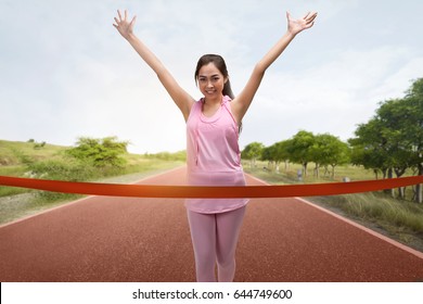 Excited Asian Woman Runner Crossing The Finish Line Of A Marathon With Blue Sky Background